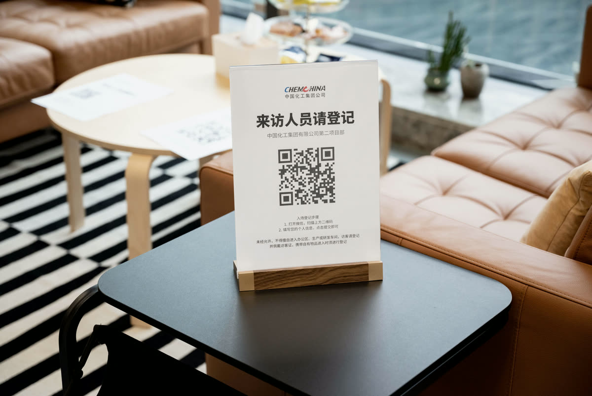 接待区桌面上的亚克力立牌,印着「来访人员请登记」和二维码